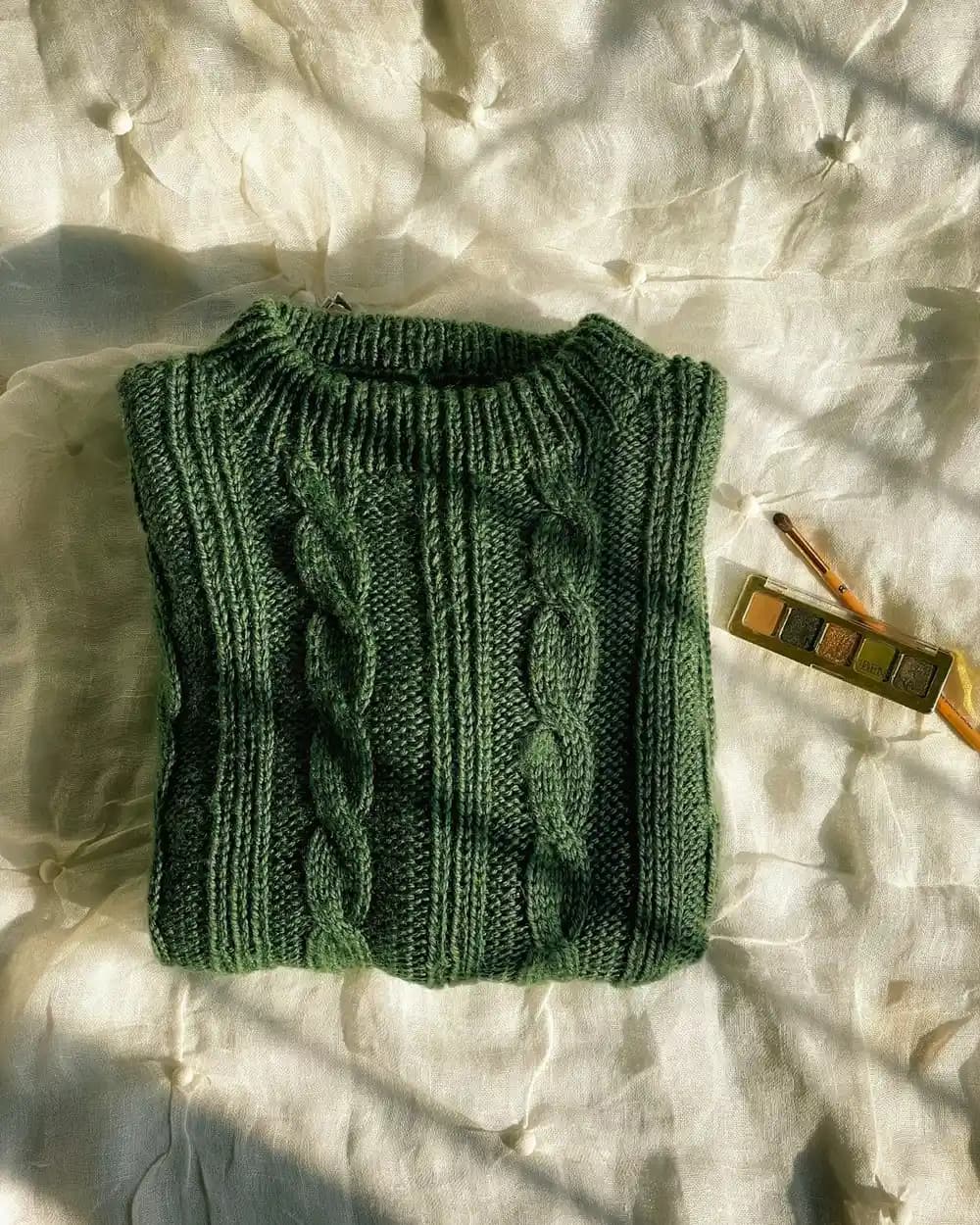 A green cable-knit sweater vest laid flat