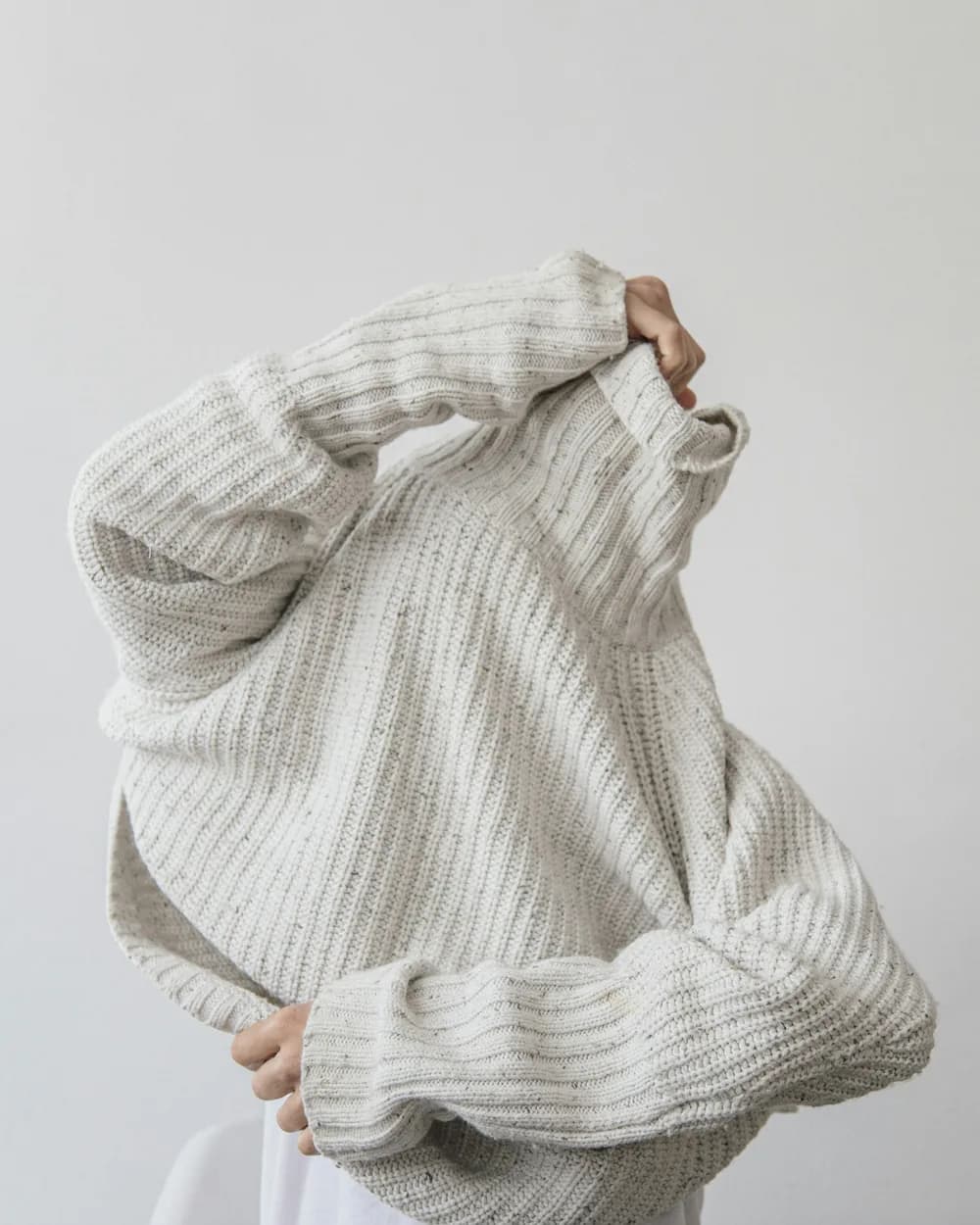 A woman pulling on a cream ribbed sweater